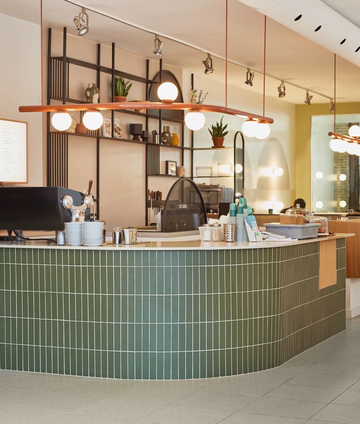 Modern Cafe Design: Stylish Curved Green Counter, Cozy Pendant Lighting, and Inviting Textured Elements