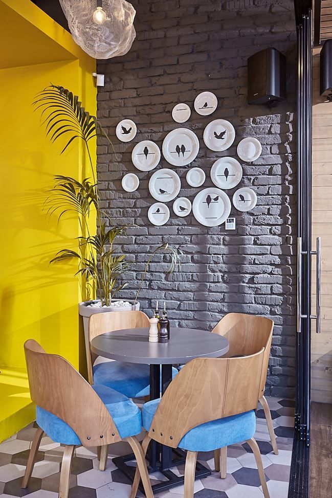 Eclectic Cafe Design: Vibrant Yellow Walls, Rustic Gray Brick, and Stylish Decor