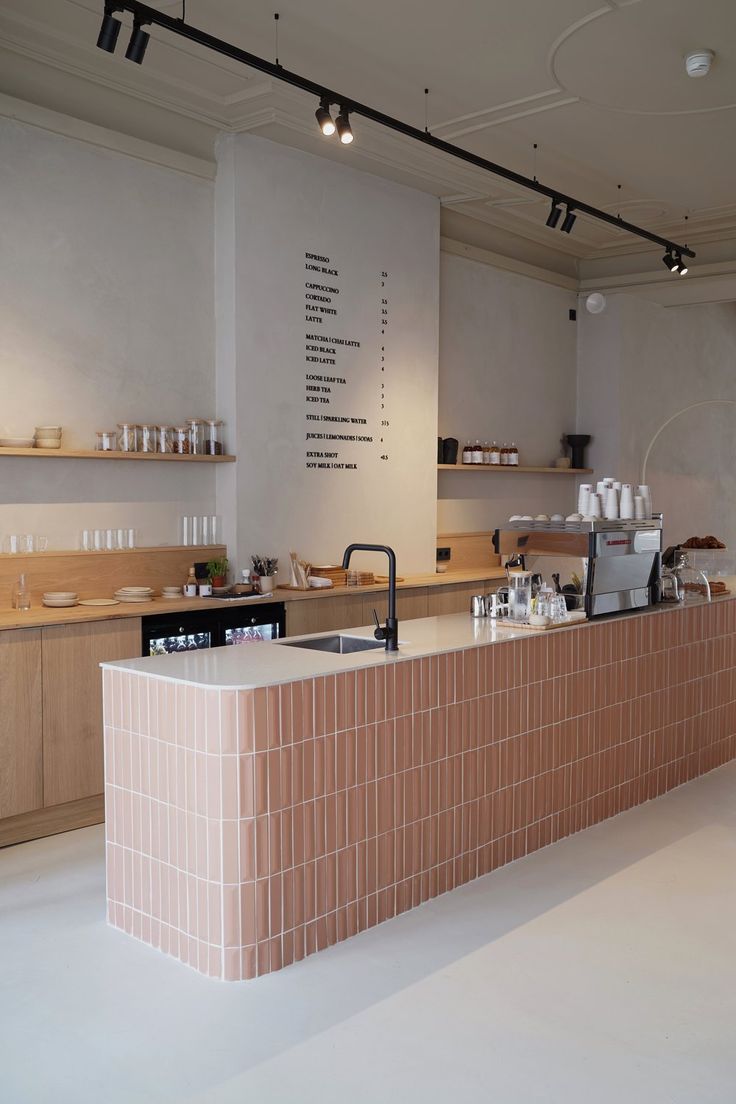 Chic Minimalist Cafe Design: Soft Pink Tile Counter, Light Wood Shelving, and Warm Ambient Lighting