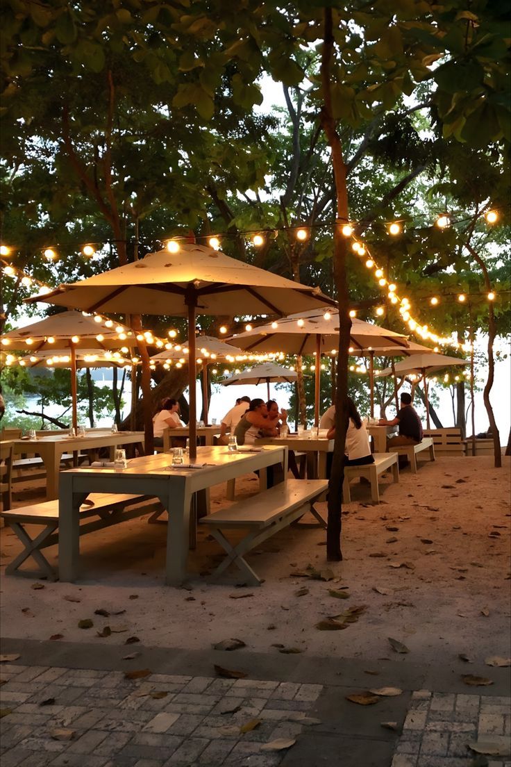 Charming Outdoor Cafe Design with Rustic Tables, Warm Lighting, and Lush Greenery